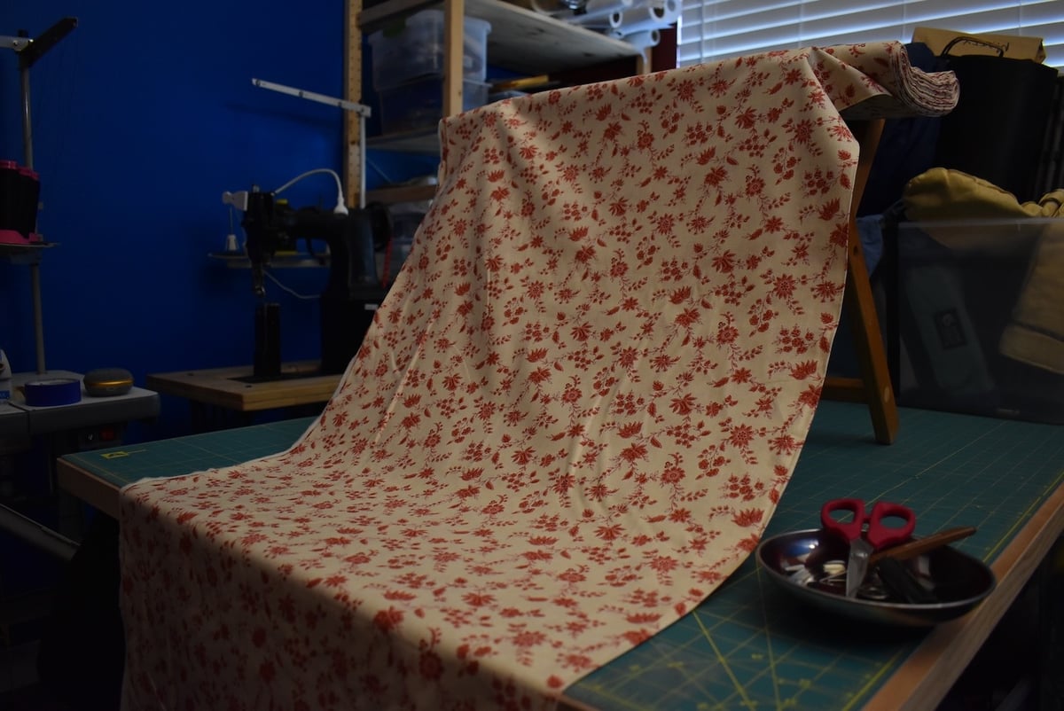 Light fabric with a small red floral motif draped over a stool.