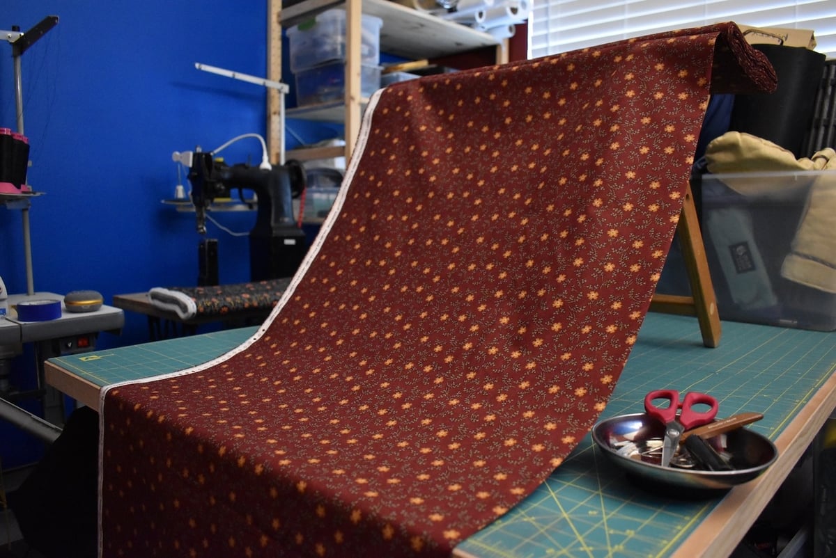 Rust colored fabric with a small floral motif draped over a stool.