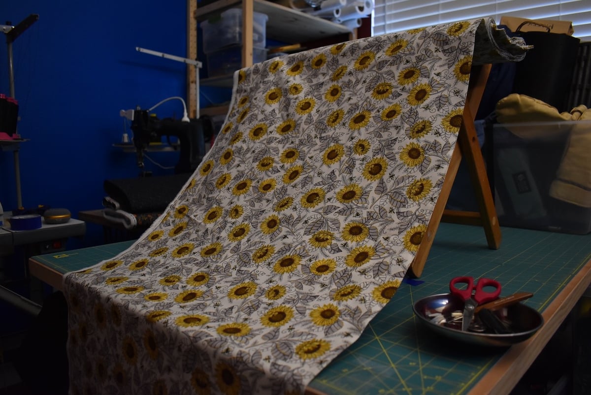 Light-colored fabric with a sunflower and bee motif draped over a stool.