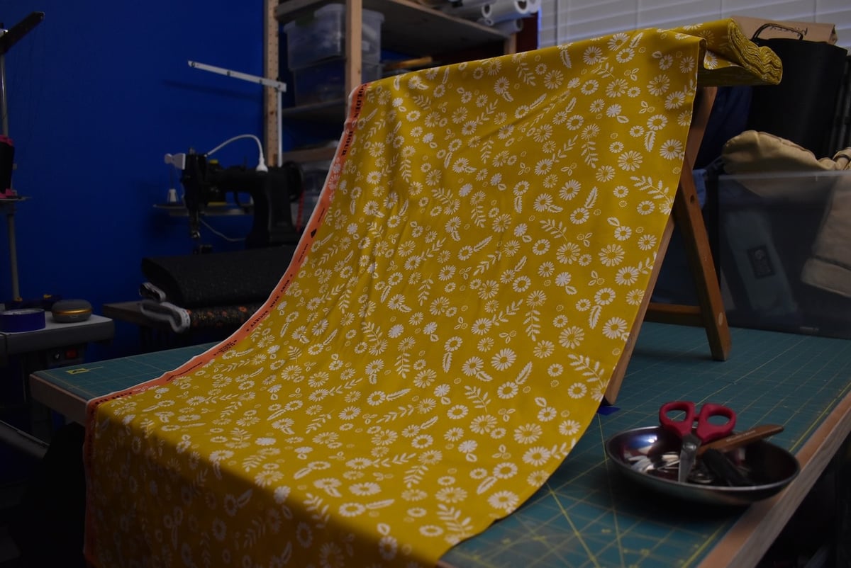 Yellow fabric with a medium floral motif draped over a stool.