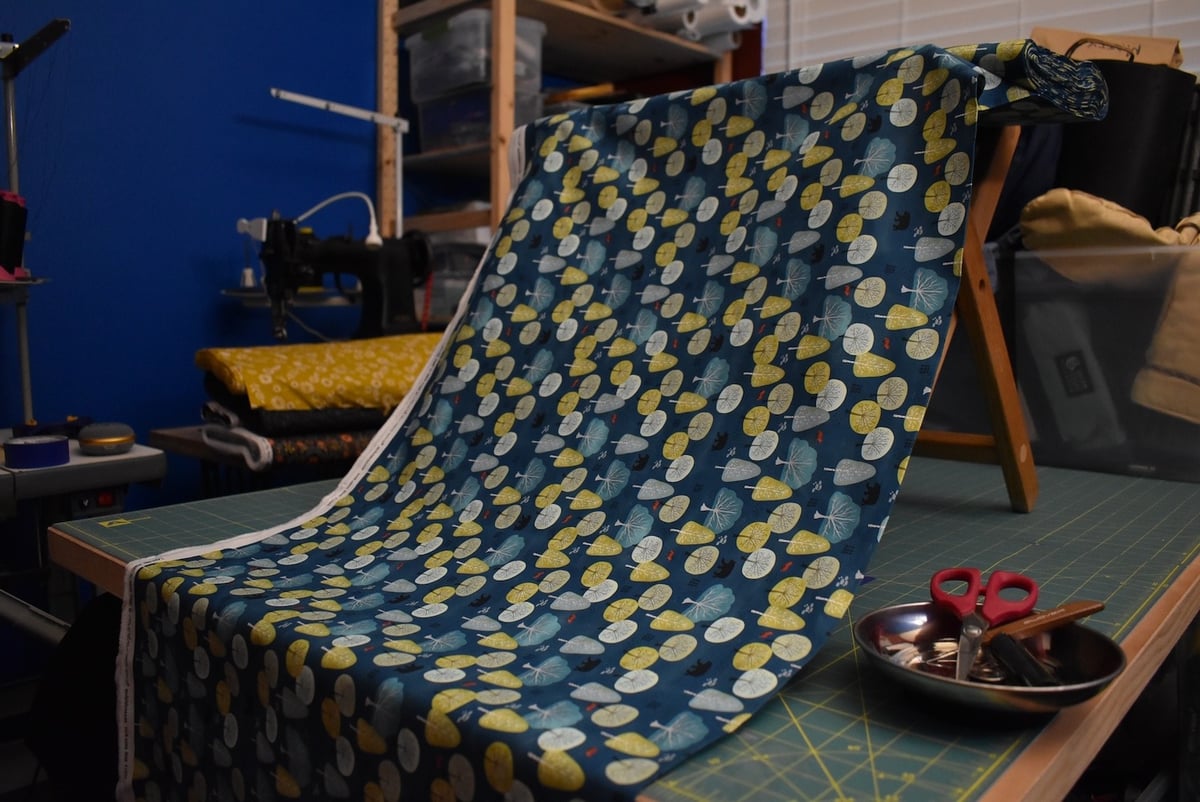 Medium blue fabric with a forest and bear motif draped over a stool.